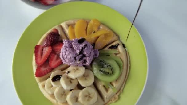 Versare lo sciroppo di cioccolato su un waffle con fette di frutta e gelato — Video Stock