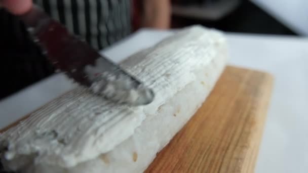 Mano extendiendo queso crema en rollo de sushi grande con un cuchillo — Vídeo de stock