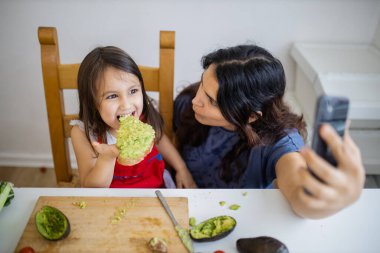 Anne ve kızı avokado yerken selfie çekiyorlar.