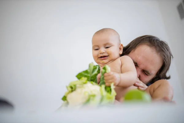Pai carinhosamente segurando e beijando sua filha bebê acima de uma mesa — Fotografia de Stock