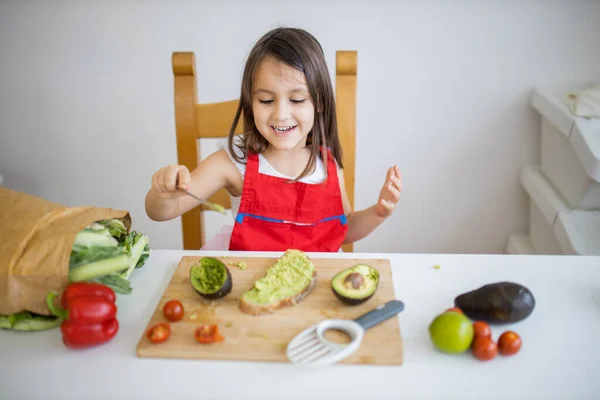 Niña en una mesa extendiendo aguacate sobre una rebanada de pan — Foto de Stock