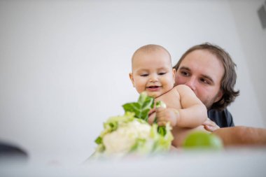 Baba sevgi dolu bir şekilde küçük kızını masanın üstünde öpüyor.