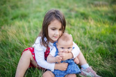 Sevimli küçük kız çimenlerde oturup bebeğe sarılıyor.