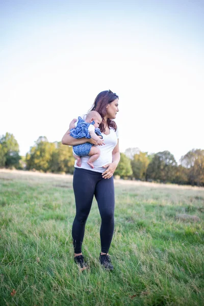Glückliche Frau steht auf dem Gras und hält ihr Baby — Stockfoto