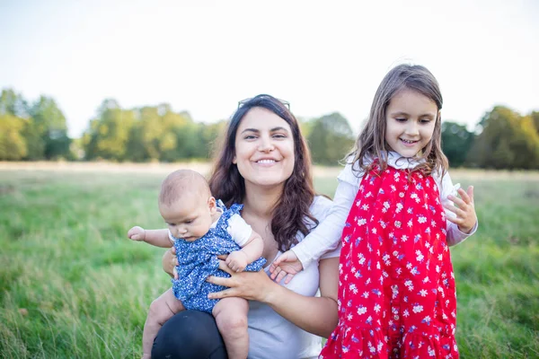 Donna felice e le sue figlie sedute sull'erba — Foto Stock