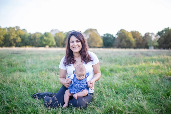 Donna felice seduta sull'erba e che tiene il suo bambino — Foto Stock