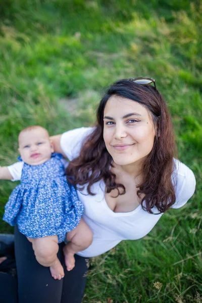 Mujer feliz sentada en la hierba con su bebé — Foto de Stock