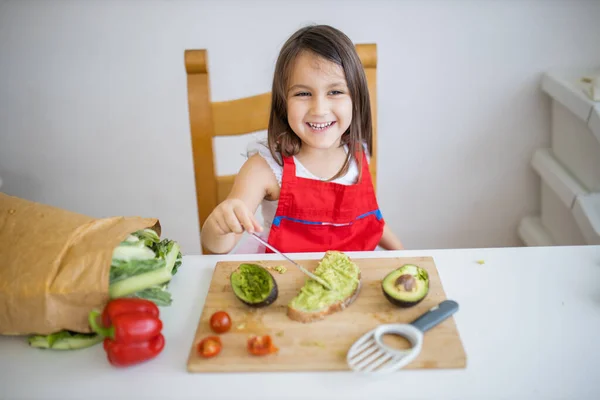 Niña en una mesa extendiendo aguacate sobre una rebanada de pan — Foto de Stock