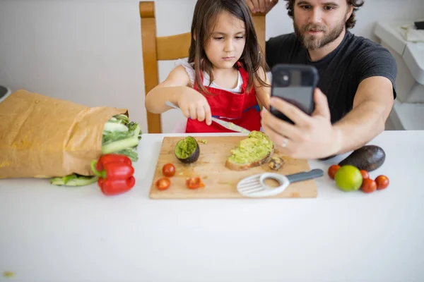 Father and daughter taking a selfie while cutting an avocado