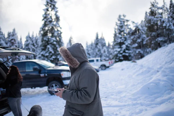 Hombre encapuchado sosteniendo un control remoto con un bosque nevado como fondo —  Fotos de Stock