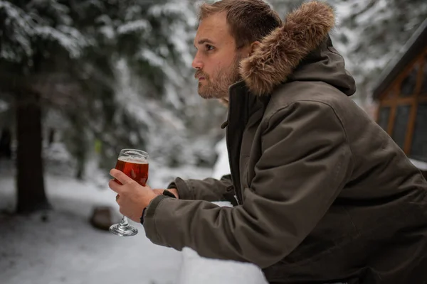 Arka planda karlı bir ormanla tırabzana yaslanan bir adam