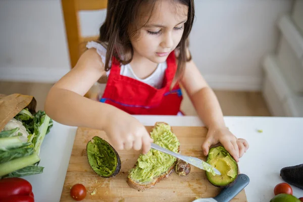 Menina em uma mesa espalhando abacate em uma fatia de pão — Fotografia de Stock