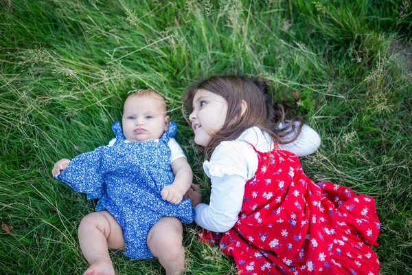Söt liten flicka och baby liggande på gräset — Stockfoto
