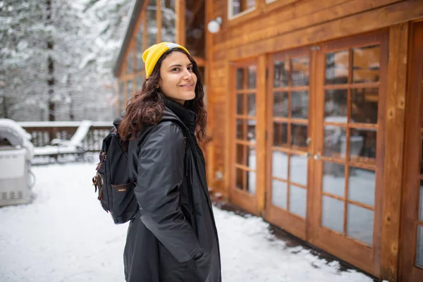 Kar kaplı bir balkonda omzunun üzerinden gülümseyen bir kadın.