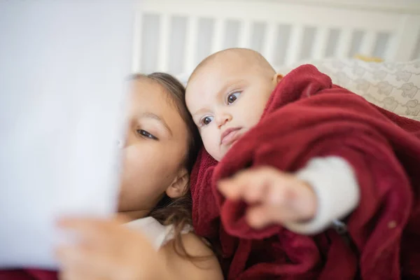 Schattig klein meisje en baby bedekt met een rode deken — Stockfoto