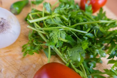 Ahşap bir masada kişniş, domates, soğan ve biber.