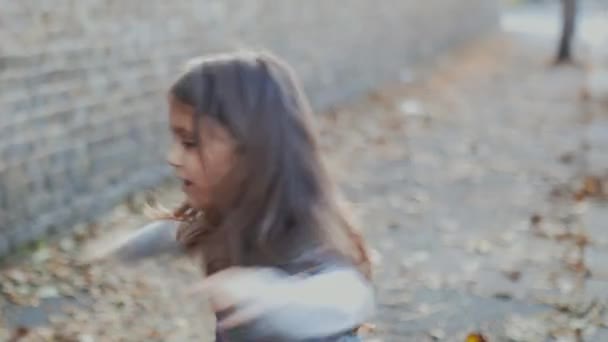 Ευτυχισμένο κοριτσάκι που παίζει σε έναν φθινοπωρινό δρόμο — Αρχείο Βίντεο