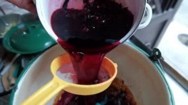 Jamaika 'nın çiçek suyunu süzgeçten geçirip büyük bir tencereye döküyor.