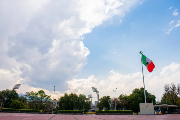 在公众广场上飘扬的墨西哥国旗，背景是多云的天空 — 图库照片