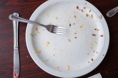 Ahşap bir masanın üstündeki boş beyaz tabakta çatal bıçak takımı.