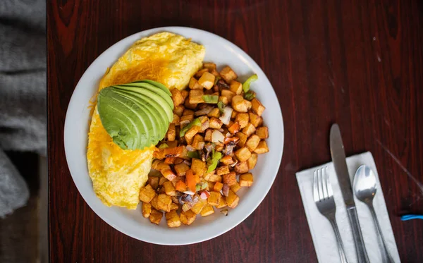 Omelette, roasted potatoes and avocado slices on a white plate