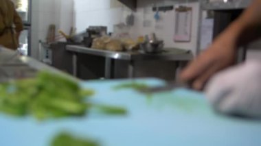 Eldivenli eller mavi kesme tahtasındaki biber dilimlerini yavaşça kesiyor.