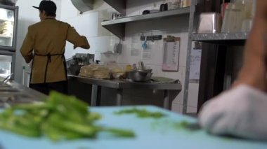 Eldivenli eller mavi kesme tahtasındaki biber dilimlerini yavaşça kesiyor.