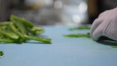 Eldivenli eller mavi kesme tahtasındaki biber dilimlerini yavaşça kesiyor.