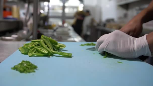 Mãos enluvadas cortando lentamente fatias de pimenta na tábua de corte azul — Vídeo de Stock