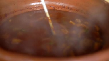 Sıcak et yahnisini karıştıran ve beyaz bir kasede servis eden kişi.