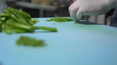 Eldivenli eller mavi kesme tahtasındaki biber dilimlerini yavaşça kesiyor.