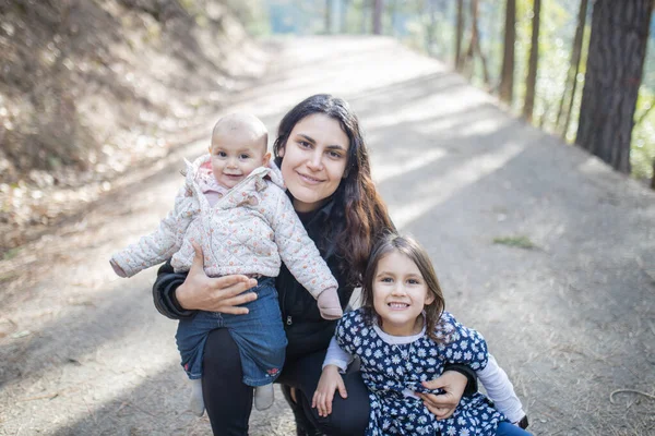 Mujer feliz sosteniendo a sus adorables hijas jóvenes en el bosque — Foto de Stock