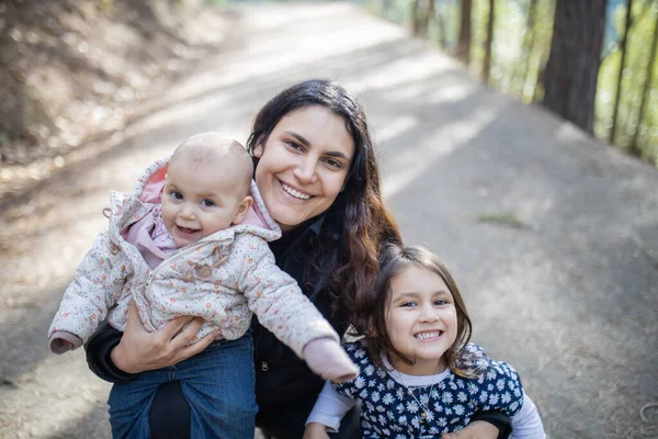 Mujer feliz sosteniendo a sus adorables hijas jóvenes en el bosque — Foto de Stock