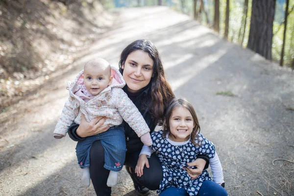 Mujer feliz sosteniendo a sus adorables hijas jóvenes en el bosque — Foto de Stock