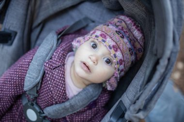 Bebek arabasında yün şapka takan sevimli ve meraklı bir bebek.