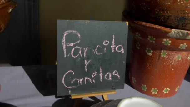 Μαύρη πινακίδα με ισπανικό κείμενο και πήλινα αγγεία σε ένα τραπέζι — Αρχείο Βίντεο