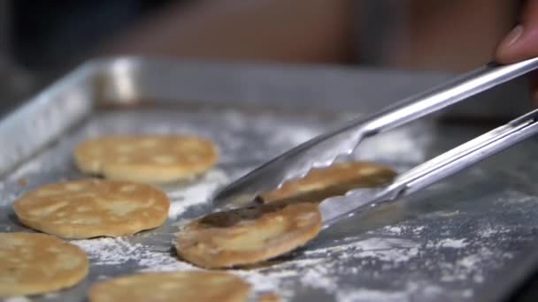 Tongs grabbing cookies from a flour-covered steel tray — Stock Video