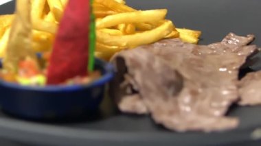 Renkli tortilla dilimleri, patates kızartmaları ve siyah tabakta ince biftek.