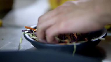 Siyah bir kasede rendelenmiş sebzeleri karıştıran erkek eller.