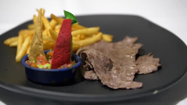 Barevné plátky tortilly, hranolky a tenký steak na černém talíři — Stock video