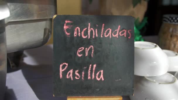 Metallkruka och svart skylt med rosa spansk text på ett bord — Stockvideo
