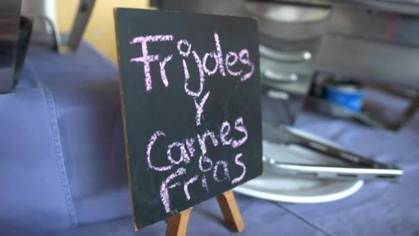 Ustensiles de cuisine et enseigne noire avec texte espagnol rose sur une table — Video