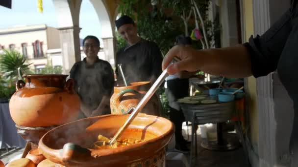 Счастливые латиноамериканские повара, стоящие за глиняными горшками горячего тушеного мяса свинины — стоковое видео