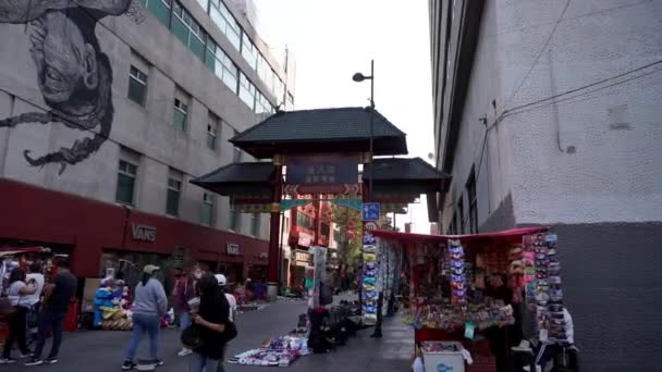 Mensen met gezichtsmaskers lopen voor de ingang van Chinatown. — Stockvideo