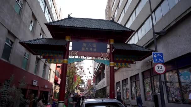 Lidé v obličejových maskách kráčejí před vchodem do čínské čtvrti — Stock video