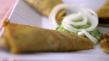 Meksika sepeti tacoları ve beyaz tabakta soğan dilimleri.