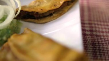 Meksika sepeti tacoları ve beyaz tabakta soğan dilimleri.