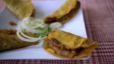 Meksika sepeti tacoları ve beyaz tabakta soğan dilimleri.