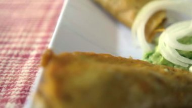 Meksika sepeti tacoları ve beyaz tabakta soğan dilimleri.