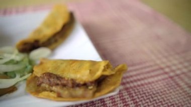 Meksika sepeti tacoları ve beyaz tabakta soğan dilimleri.